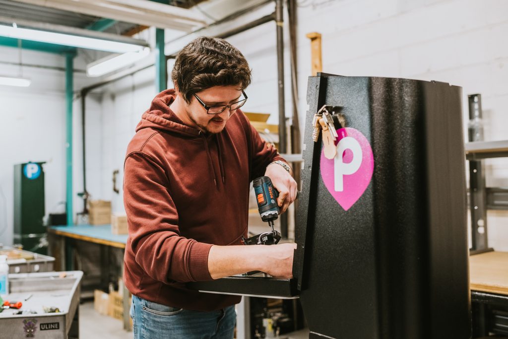 A worker using a power tool to put together a parking meter.