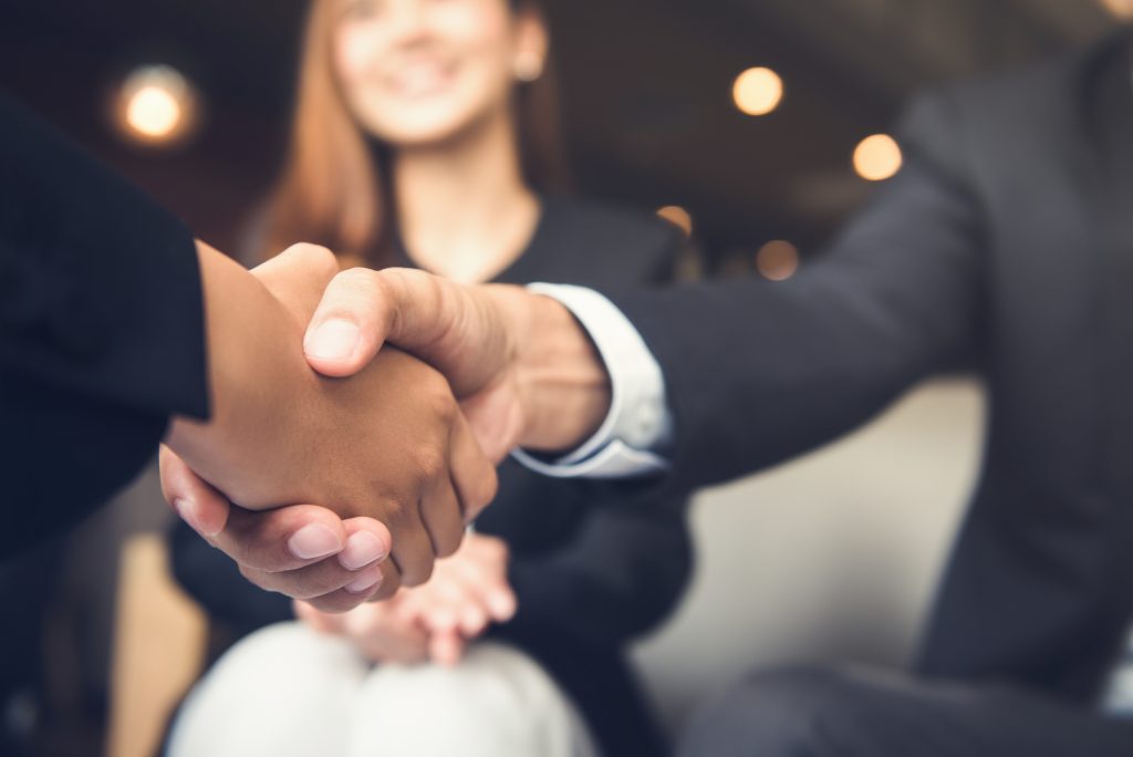 Business person shaking hands with their partner in a cafe.